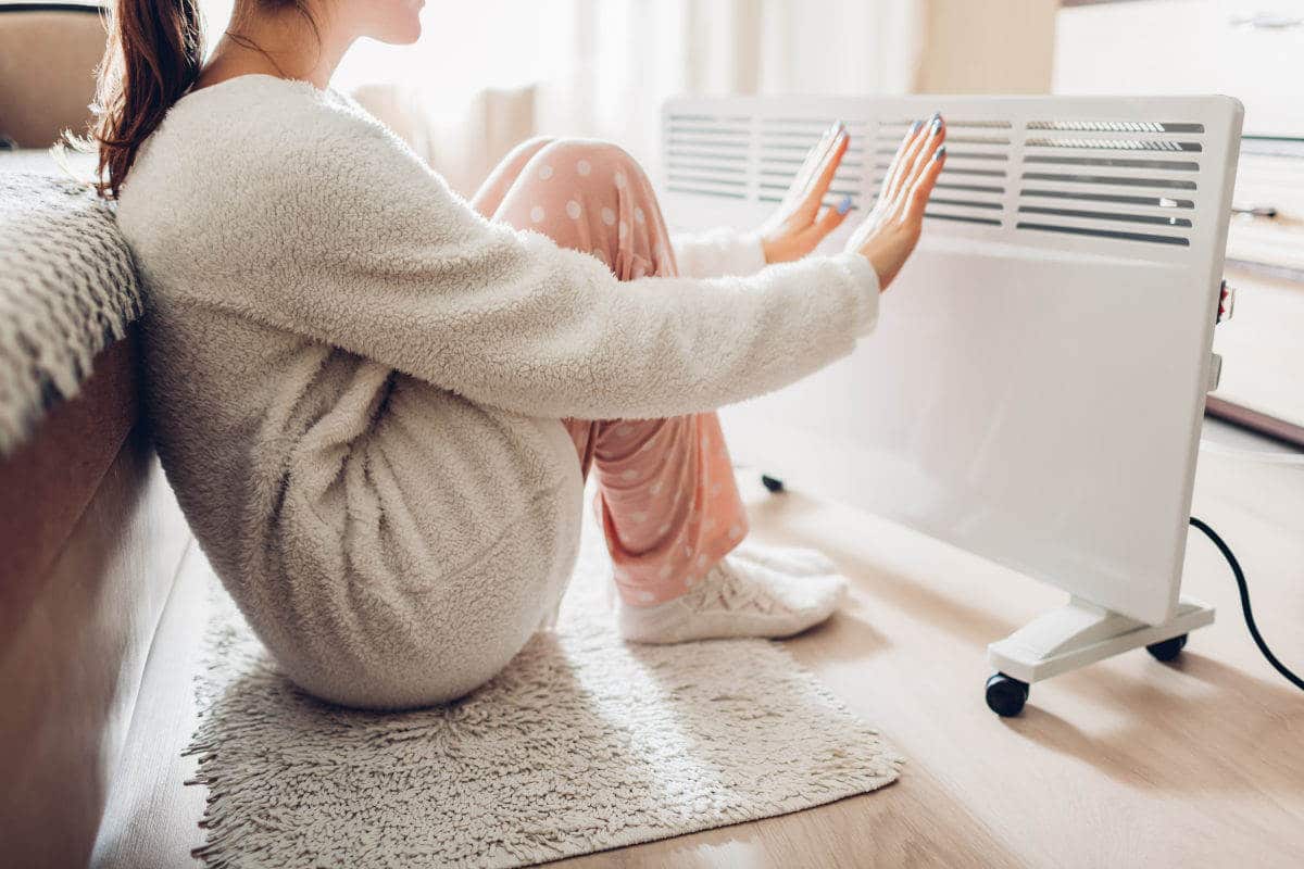 Using heater at home in winter. Woman warming her hands. Heating season. Elektroheizung