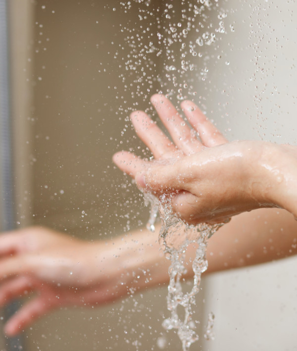 Frau dreht Dusche auf, Wasser tropft in ihre Hand