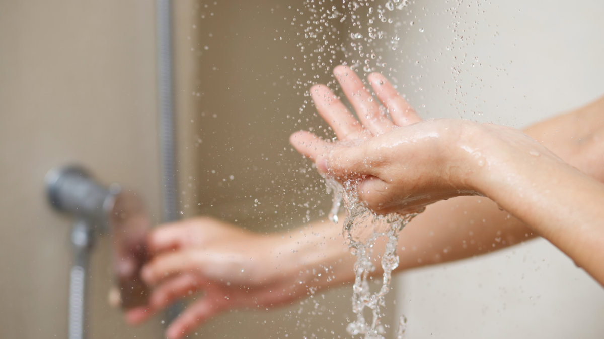 Frau dreht Dusche auf, Wasser tropft in ihre Hand